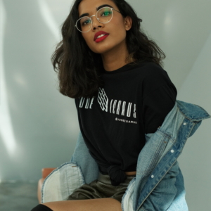 A woman sits looking at the camera, wearing a Jude Icarus Tee and a denim jacket
